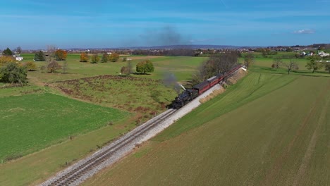 Eine-Luftaufnahme-Eines-Dampfzuges,-Der-Rauch-Bläst,-Während-Er-An-Einem-Sonnigen-Herbsttag-Durch-Landwirtschaftliche-Flächen-Fährt