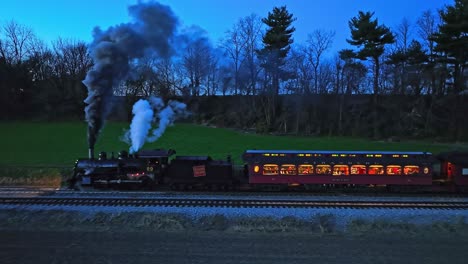 Eine-Parallele-Nachtansicht-Einer-Drohne-Eines-Dampf-Personenzuges,-Der-In-Ackerland-Anhielt-Und-Viel-Rauch-Bläst,-Während-Er-Die-Lichter-In-Den-Waggons-Sieht