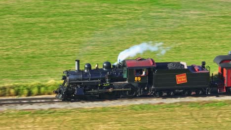 Una-Vista-Aérea-Paralela-Ampliada-De-Un-Tren-De-Pasajeros-De-Vapor-Que-Viaja-En-Una-Sola-Vía-A-Través-Del-Campo