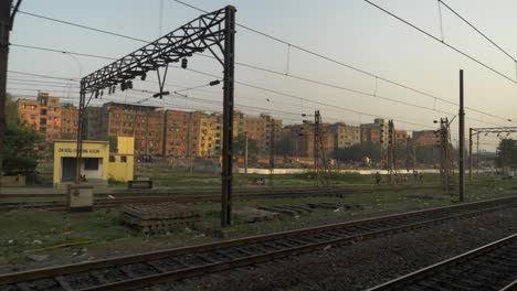 Vista-Lateral-Del-Patio-Ferroviario-Desde-Un-Tren-En-Movimiento-Que-Entra-Lentamente-En-El-Cruce-De-La-Plataforma-Ferroviaria-Con-Un-Antiguo-Edificio-Rústico-Al-Fondo