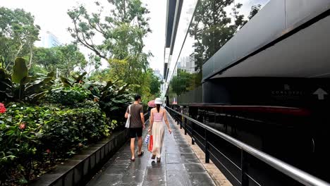 Detrás-De-La-Gente-Caminando-Por-Un-Tren-Moderno-En-Una-Calle-Estrecha-Y-Exuberante,-Sinapur