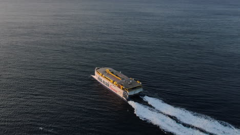 Fantástica-Toma-Aérea-Lateral-Y-A-Alta-Velocidad-De-Un-Ferry-Que-Sale-Del-Puerto-De-Agaete-Hacia-Tenerife-Durante-La-Puesta-De-Sol