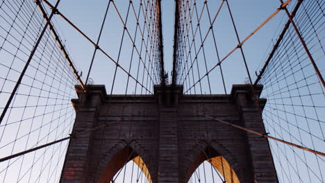 Parallel-cables-and-tower-of-Brooklyn-Bridge,-golden-sunlight-and-flare,-Tilt-Up