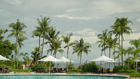 Huéspedes-Del-Hotel-Junto-A-La-Piscina-Con-Tumbonas,-Sombrillas-Y-Palmeras