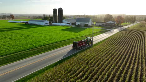 John-Deere-cab-tractor-and-manure-spreader-drives-on-road-in-autumn-sunset