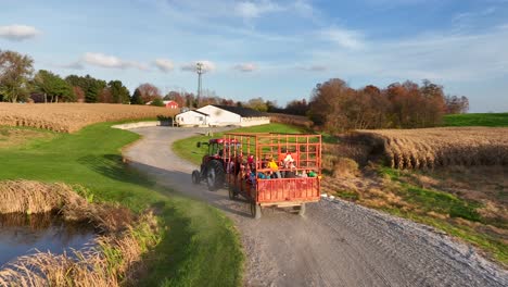 Luftdrohnenaufnahme-Von-Kindern,-Die-Während-Der-Erntezeit-Im-Herbst-Auf-Einem-Von-Einem-Traktor-Gezogenen-Wagen-Eine-Heufahrt-Auf-Dem-Bauernhof-Genießen