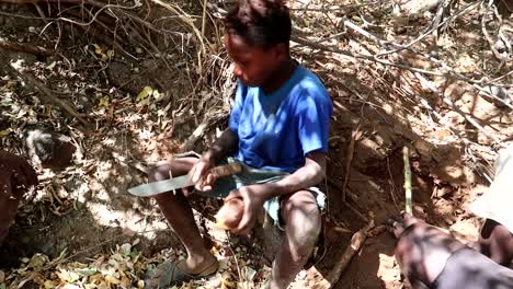 Toma-Completa-Del-Niño-De-La-Tribu-Hadzabe-Pelando-La-Raíz-Del-árbol-Boabab-Sentado-En-El-Suelo