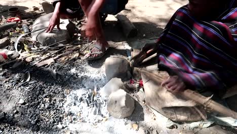 Hombre-De-La-Tribu-Datoga-Soplando-Brasas-Con-Un-Rudimentario-Sistema-Artesanal-Para-Derretir-Metal