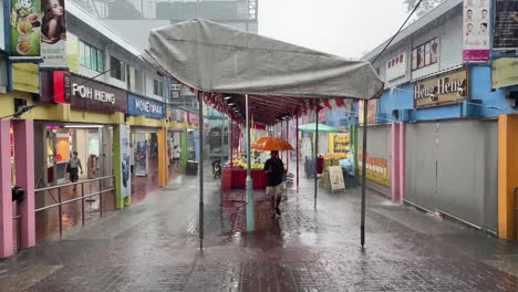 Man-carries-an-orange-umbrella-and-walks-under-the-tentage-in-Ang-Mo-Kio,-the-rainy-season-in-Singapore