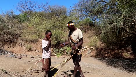 Hadzabe-Stamm-Lokaler-Mann-Und-Junge,-Der-Beeren-Von-Einem-Ast-In-Der-Afrikanischen-Savanne-Isst