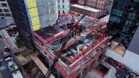 Vista-Aérea-De-Una-Grúa-Que-Levanta-Materiales-A-Un-Sitio-De-Construcción-En-La-Zona-Urbana-De-Nueva-York