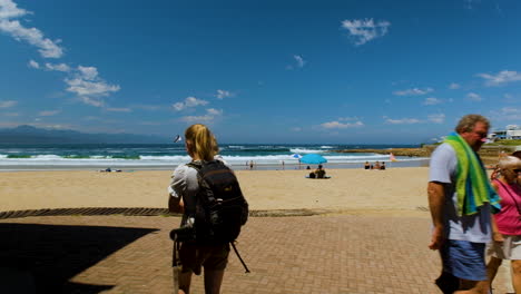 Toma-Panorámica-En-El-Popular-Paseo-Marítimo-De-La-Playa-Central-Con-Bañistas,-Plettenberg-Bay