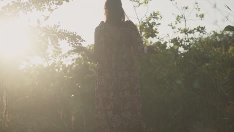 Mujer-Mirando-Las-Plantas-Y-Levantando-Las-Manos-Mientras-El-Sol-Brilla-Detrás-De-Las-Plantas-Causando-Contraluz