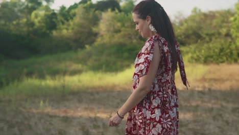 Woman-in-a-dress-calmly-walking-while-looking-around-at-the-grass-and-trees