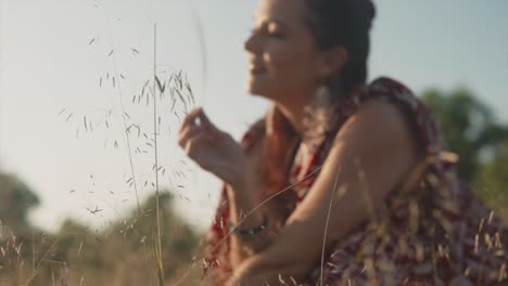 Mujer-Borrosa-Con-Un-Vestido-Sonriendo-Y-Jugando-Con-Plantas-En-El-Campo-Durante-El-Día