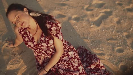 Mujer-Sentada-En-La-Triste-Playa-Con-Un-Vestido-Con-Los-Ojos-Cerrados-Disfrutando-De-La-Luz-Del-Sol