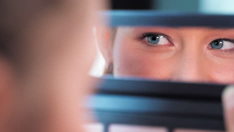 A-closeup-view-of-a-woman's-blue-eyes-looking-in-her-pocket-mirror