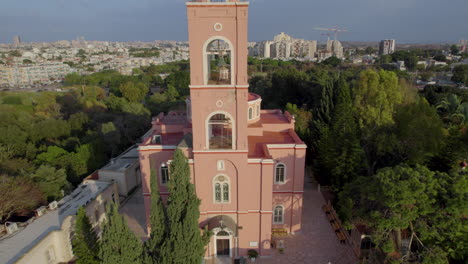 Das-Aufstehen-Enthüllt-Eine-Wunderschöne-Rosafarbene-Kirche,-Die-Von-Bäumen-Umgeben-Ist---Drohnenaufnahme