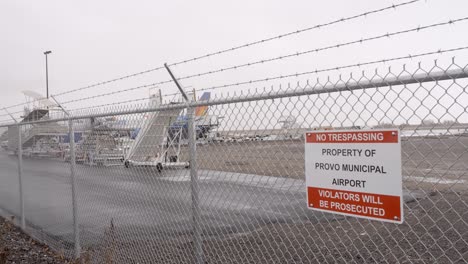 No-Trespassing-sign-on-the-fence-at-Provo-Municipal-Airport-with-a-Allegiant-Airlines-plane-at-the-departure-gate-during-snow,-sleet-and-rain