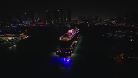 Vista-Aérea-Trasera-De-Un-Enorme-Barco-Que-Llega-A-La-Terminal-De-Cruceros-En-El-Puerto-De-Miami-Por-La-Noche