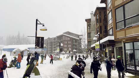 Revelstoke-Mountain-Resort-Village,-British-Columbia-after-a-day-on-the-mountain-with-plenty-of-skiers-and-snowboarders-leaving-and-snow-falling