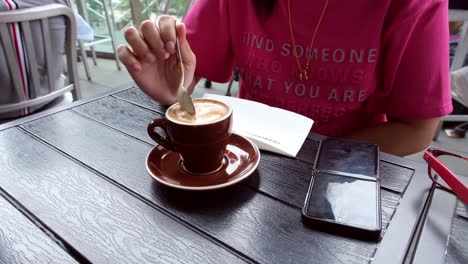 Una-Persona-Tomando-Una-Taza-De-Café-Con-Una-Camisa-Rosa-Suelta-Y-Un-Teléfono-En-La-Mesa