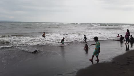 Los-Niños-Juegan-Con-Una-Pelota-De-Fútbol-En-La-Playa,-Divirtiéndose-En-El-Agua-Del-Mar-De-Bali,-Indonesia,-Saba,-Gianyar,-Arena-Negra,-Amistad-Infantil,-Sudeste-Asiático