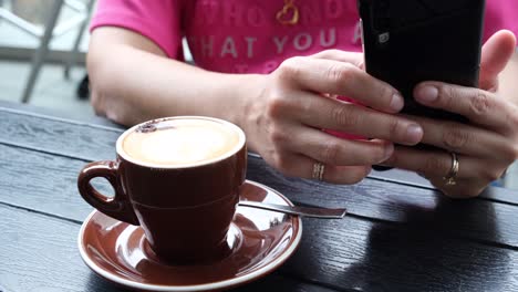 Eine-Person,-Die-Ein-Telefon-Hält,-Während-Sie-Eine-Tasse-Kaffee-Trinkt