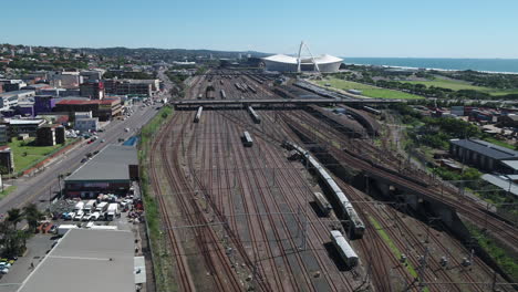 Toma-Aérea-De-Drones-De-La-Estación-De-Tren-De-Durban-Con-El-Estadio-Moses-Mabhida-En-El-Fondo-Y-El-Océano-índico