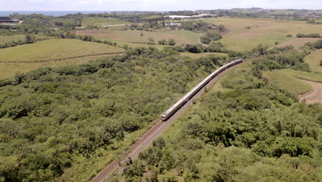 Toma-Aérea-De-Drones-De-Un-Tren-De-Pasajeros-En-Sudáfrica-Que-Viaja-A-Través-De-Colinas-Verdes