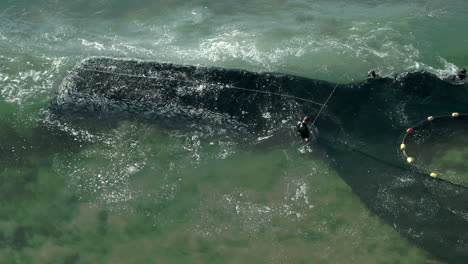 Aerial-drone-shot-off-a-drag-net-full-of-sardines-and-pilchard-fish-in-the-waves