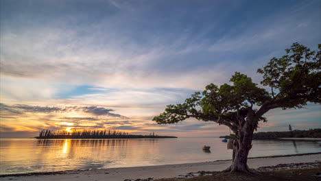 Sunset-to-dark-timelapse-of-beautiful-tree,-beach,-water,-island,-anchored-boat-near-Isle-of-Pines