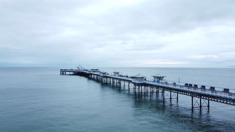 Llandudno-pier-historic-Victorian-wooden-seaside-landmark-aerial-view-low-following-idyllic-boardwalk