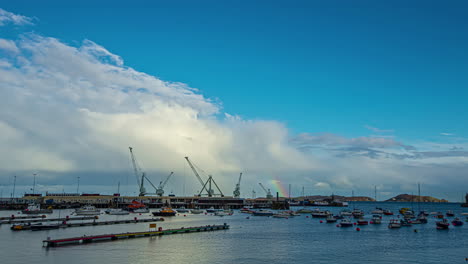 Cinematic-timelapse-of-a-rainbow-rising-through-St-Peter-Port-of-Guernsey-with-many-cruises-sailing-across-the-sea-and-clouds-rising-above