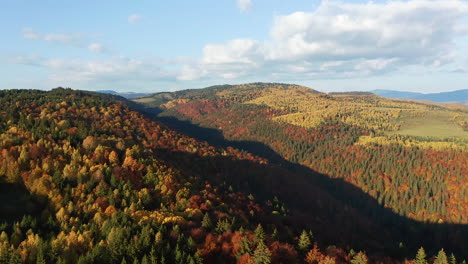 Aufsteigende-Aufnahme-Aus-Der-Luft-Von-Gebirgsausläufern,-Die-Mit-Herbstlichen-Wäldern-Bedeckt-Sind