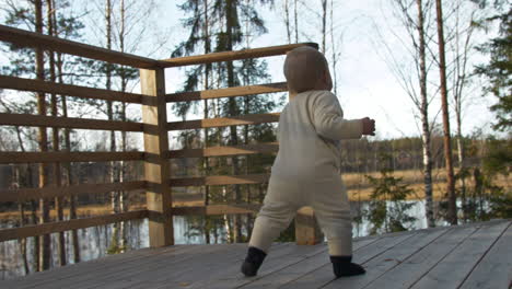 Unstable-baby-walking-on-wooden-deck-in-autumn-landscape