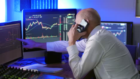 A-busy-forex-stock-cryptocurrency-trader-is-talking-on-the-phone-in-the-office-while-analyzing-trading-charts