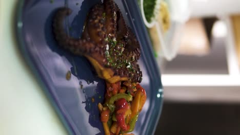 Vertikale-Zeitlupenaufnahme-Eines-Köstlichen-Gerösteten-Tintenfischs,-Garniert-Mit-Verschiedenen-Gemüsesorten,-Die-In-Einem-Teuren-Restaurant-Mit-Olivenöl-Verfeinert-Wurden