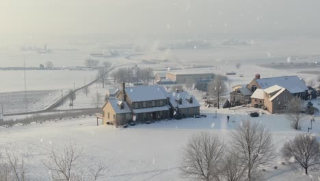 Aerial-establishing-shot-of-home-and-orchard-farmland-during-winter-snowstorm