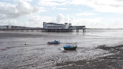 Last-section-of-the-Grand-Pier-Weston-Super-Mare-with-a-cloudy-and-blue-sky-in-the-background,-small-fishing-boats-moored-in-the-sand-banks
