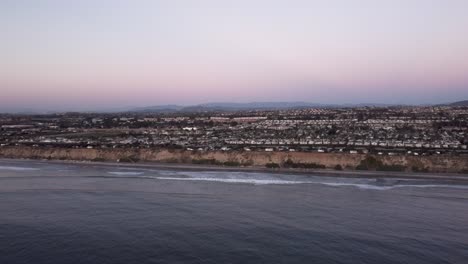 A-beautiful-aerial-drone-shot,-flying-towards-the-coast-with-a-view-of-a-town,-the-horizon,-and-mountains,-Carlsbad-State-Beach---California