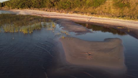 Aerial-shot-of-woman-walking-on-natural-lake-shore-with-sandy-beach-during-sunset-time---Laguna-Negra,Uruguay