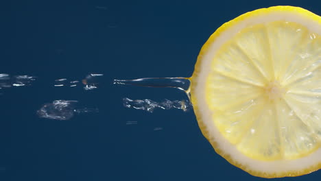 Vertikale-Zeitlupenmakroaufnahme-Von-Fließendem-Wasser-Aus-Zitronenscheibe-Auf-Blauschwarzem-Hintergrund