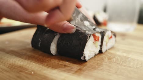 Person-cut-homemade-sushi-into-small-rolls,-close-up-view