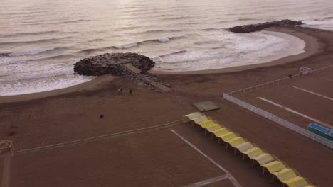 Aerial-Orbit-shot-of-People-Walking-on-sandy-beach-of-Mar-del-Plata-during-sunrise---Argentina,South-America