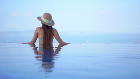 A-young-woman-with-her-back-to-the-camera-lingers-at-the-edge-of-an-infinity-pool-while-she-looks-out-to-the-ocean
