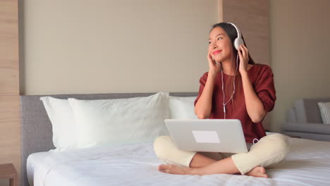 Smiling-Asia-Woman-Listen-Music-From-Laptop-With-Headphones-and-Moving-Head-in-Rhythm-of-Song,-Static-With-Copy-Space