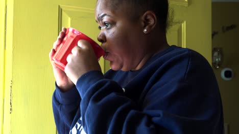 Afroamerikanerin-Vor-Gelber-Tür,-Die-Kaffee-In-Einem-Roten-Becher-Trinkt