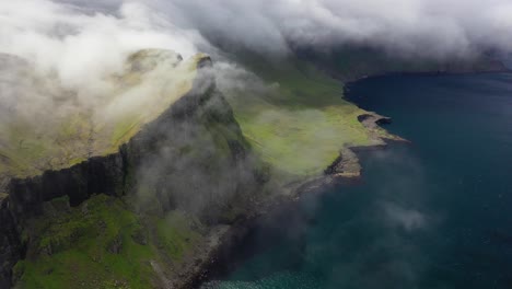 Clouds-rolling-over-coastal-cliffs-in-remote-Faroe-Islands,-high-aerial-view