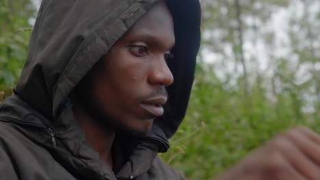 A-close-up-shot-of-an-African-man-wearing-a-hooded-coat-sitting-down-in-a-forest-in-Africa